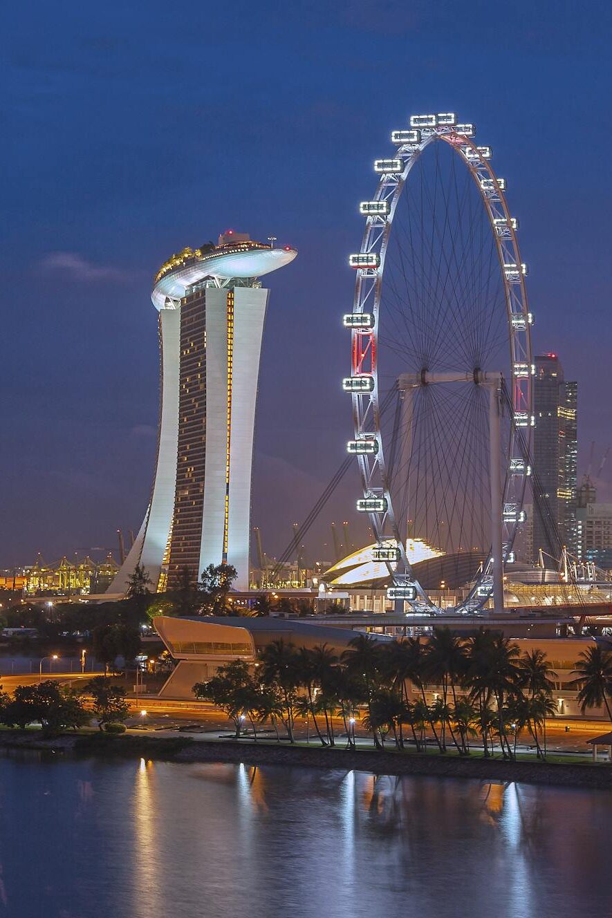 Stunning night view of Singapore with Marina Bay Sands and Ferris Wheel, reflecting city lights on water.
